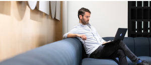 Man sitting on a blue sofa, looking at his laptop computer